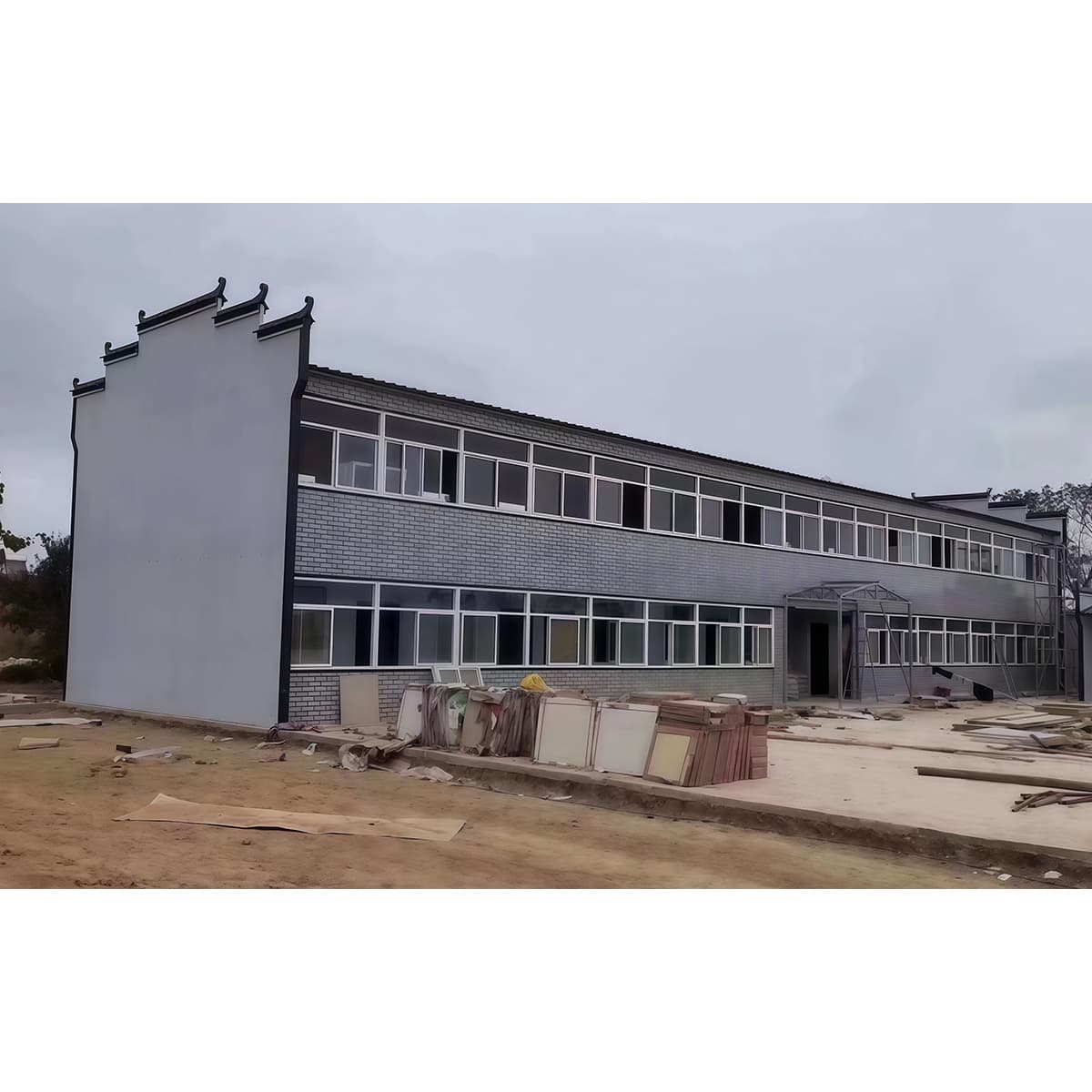 Two-storey K-Type prefabricated building under construction with structural panels staged at ground level